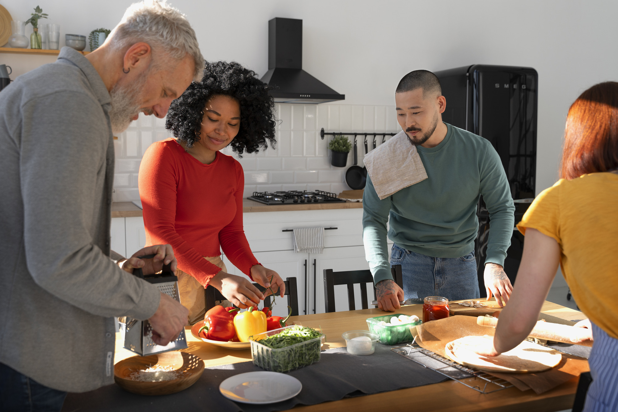 Four people preparing pizza around a kitchen table with fresh vegetables.